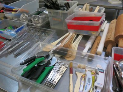 Large Quantity of Assorted Commercial Kitchen & Bakery Accessories to Include: Knives, Spreaders, Cutters, Scoops, Whisks, Sieves, Rolling Pins, Graters, Scissors & Other (As Viewed/Pictured).