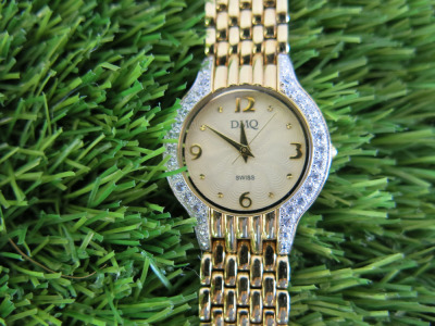 DMQ Gold Tone Ladies Wrist Watch with Gemmed Bezel. NOTE appears unworn.