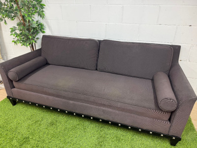 Dark Grey/Purple Upholstered Sofa with Bolster Cushions & Metallic Stud Detail on Black Wooden Leg Base. Size H78 x W210 x D90cm.